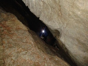 Udo, Schamane, in einer Höhle, zwischen den beiden Felsen leuchtet uns seine Stirnlampe entgegen.